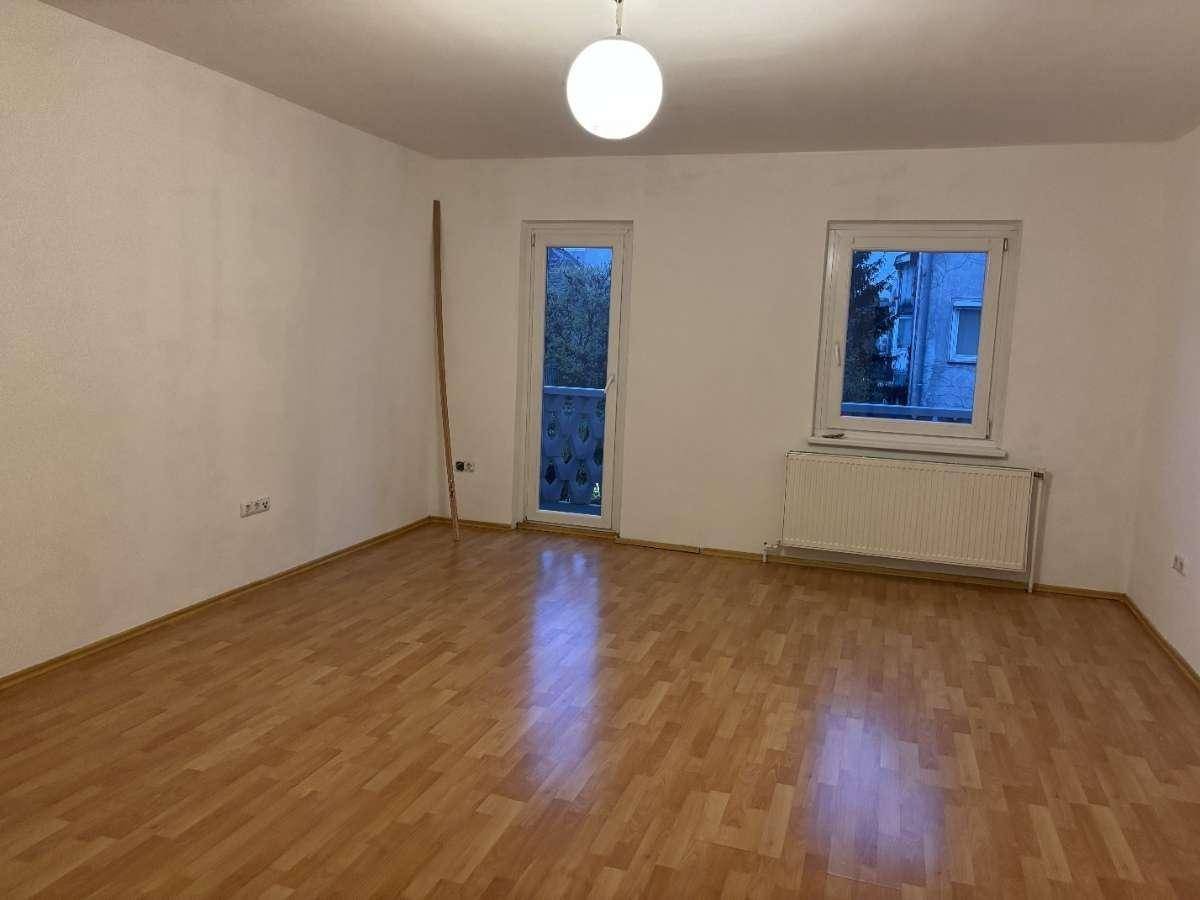 Heller Raum mit Laminatboden, Heizkörper und Zugang zu einem französischen Balkon.