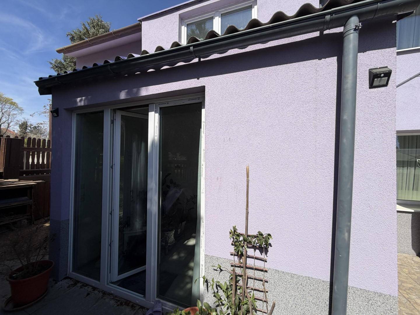 Nahaufnahme der lila Hausfassade mit einer breiten Glastür, die zum Garten führt.