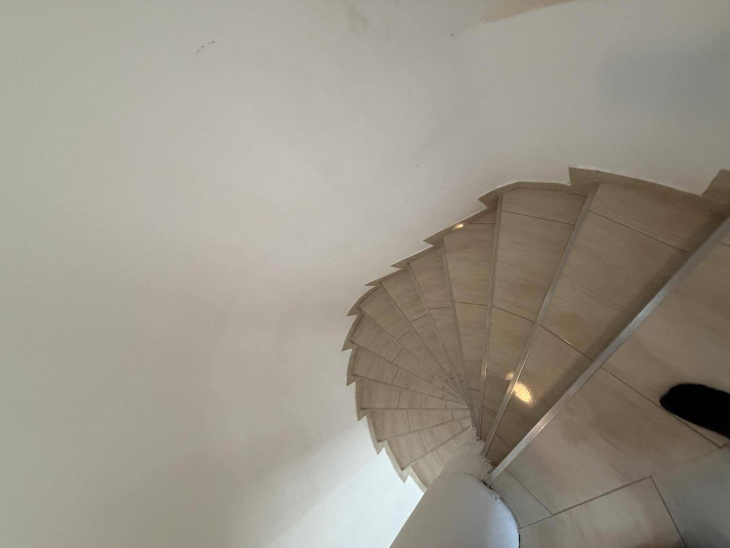 Blick von oben auf die geschwungene Wendeltreppe mit hellen Fliesen.