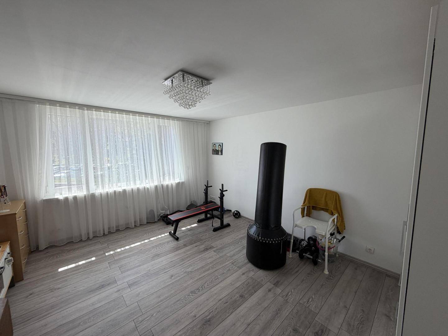 Geräumiges Schlafzimmer mit Laminatboden, großer Fensterfront und Fitnessgeräten.