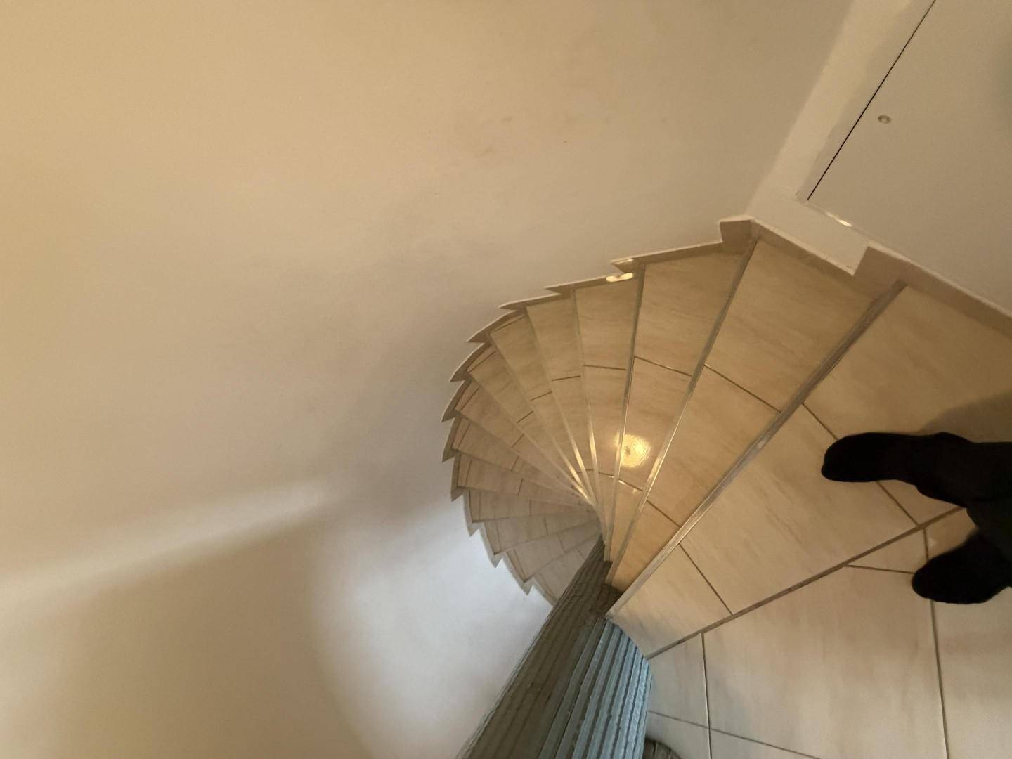 Blick von oben auf die elegant geschwungene Wendeltreppe mit hellen Fliesen.
