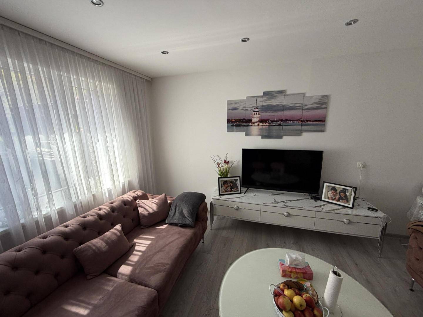 Helles Wohnzimmer mit großem Fenster, das viel Tageslicht hereinlässt, und bequemer Couch.