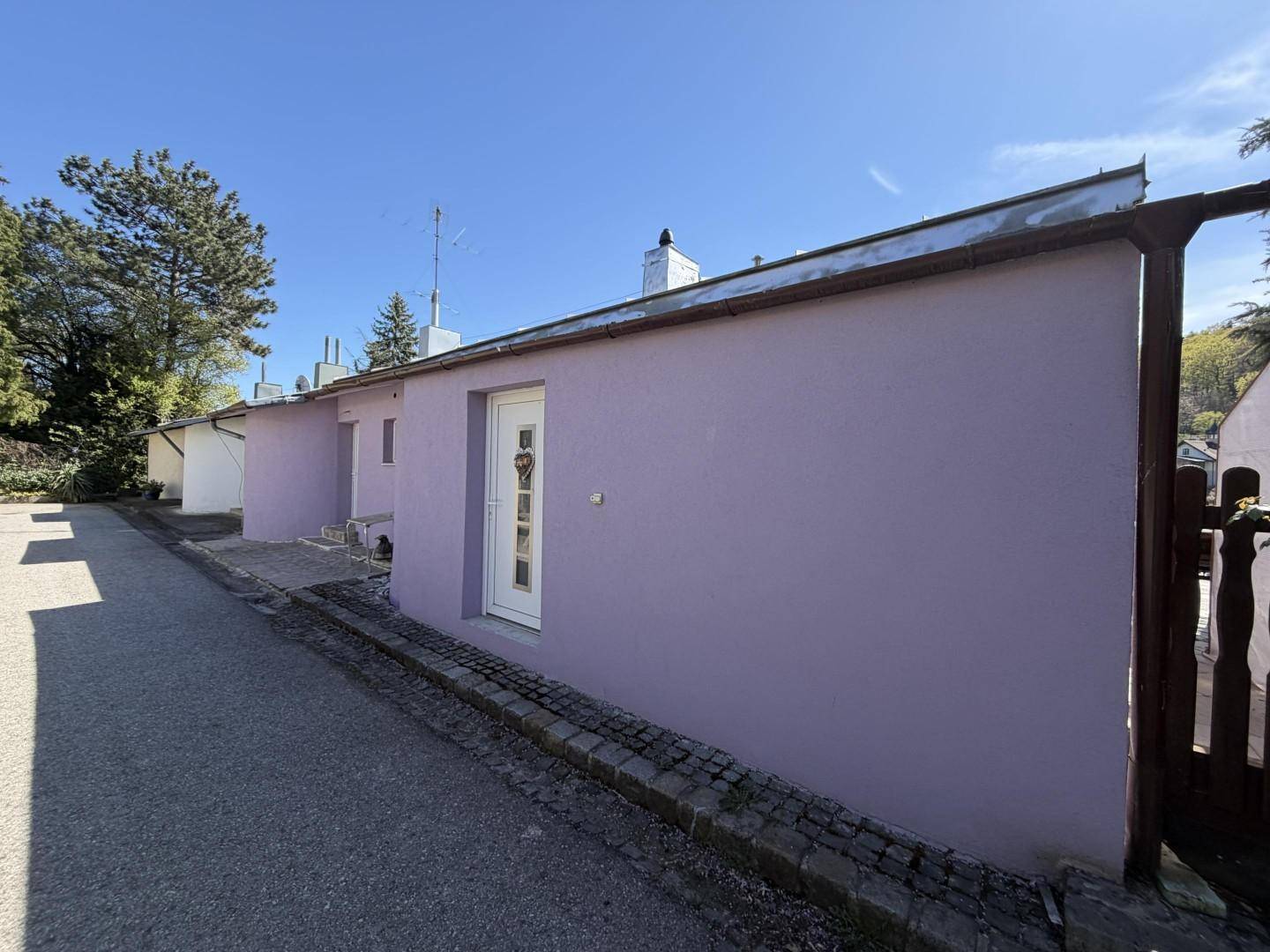 Seitenansicht des Hauses mit lila Fassade und einer gepflasterten Zufahrt.