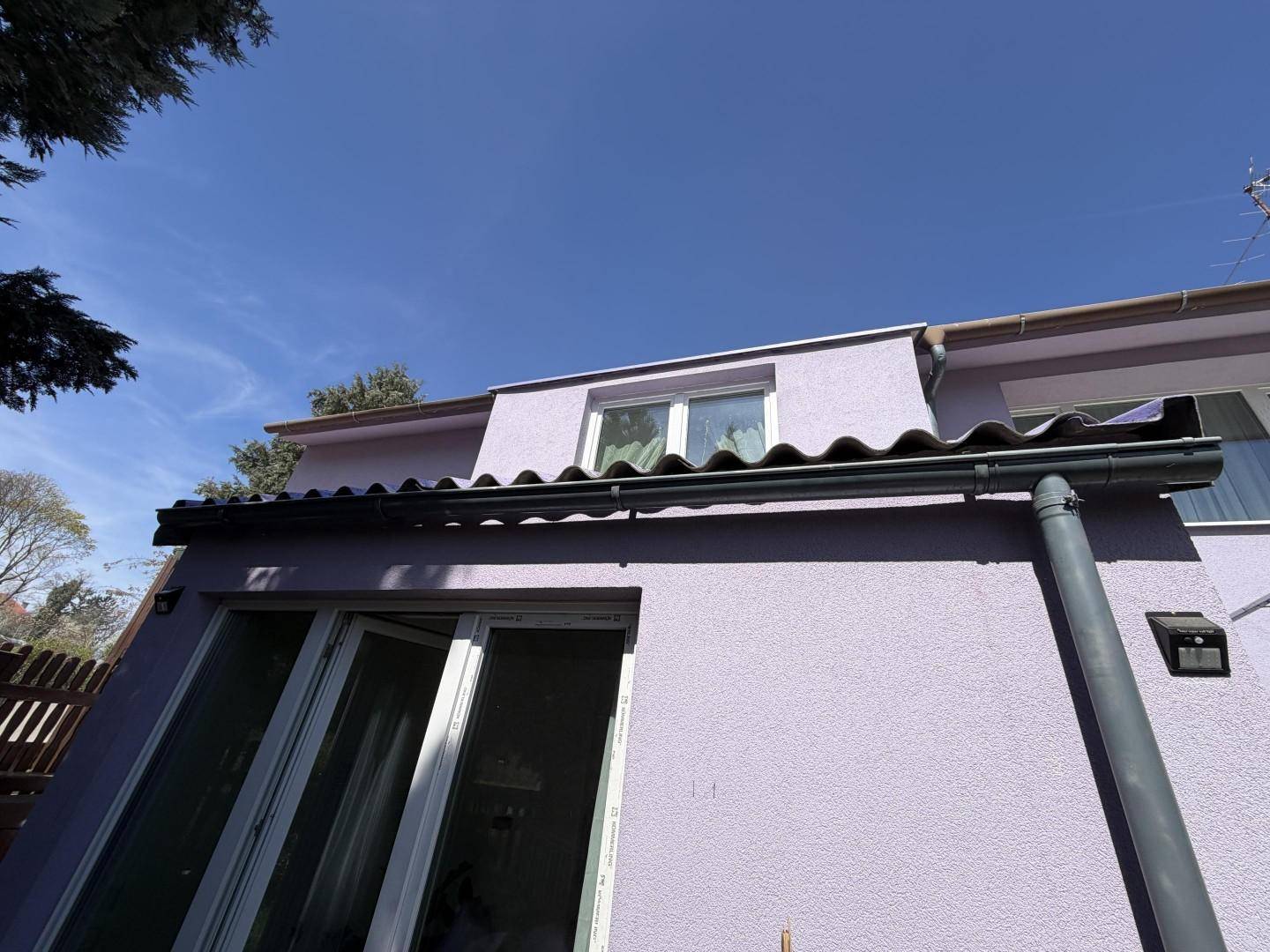 Seitenansicht des Hauses mit lila Fassade, großen Fenstern und Dachüberstand.