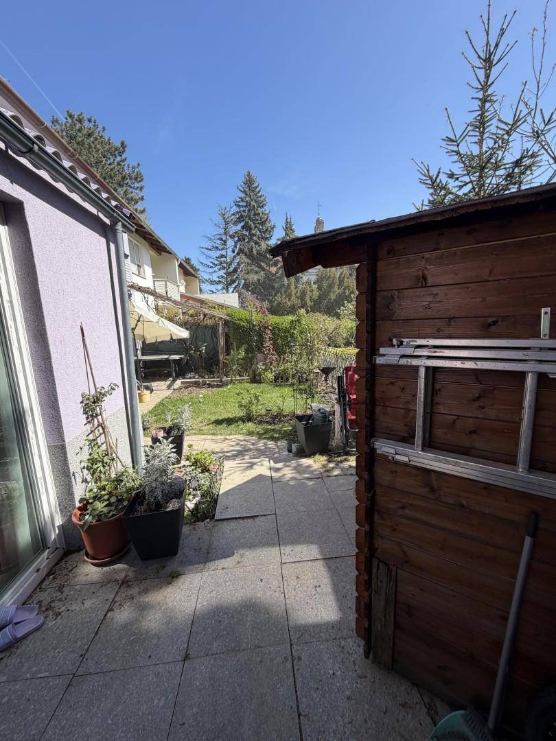 Gepflasterter Terrassenbereich mit Gartenhaus und Blick auf den grünen Garten.