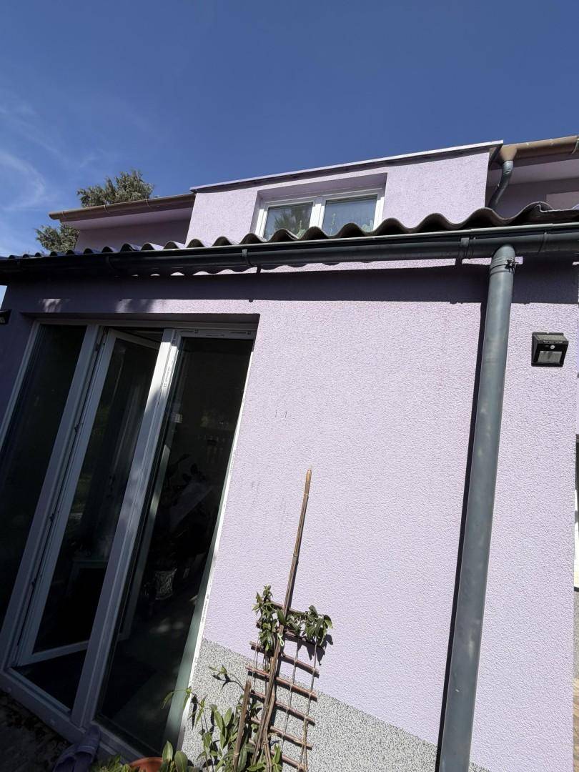 Detailansicht der lila Hausfassade mit großen Fenstertüren und einem Dachüberstand.