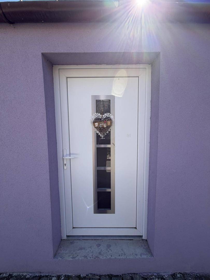 Weiße Eingangstür mit Glaseinsätzen an der lila Hausfassade.