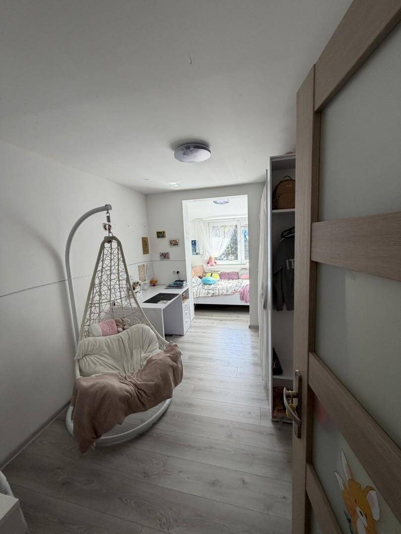Helles Kinderzimmer mit Schreibtisch, Hängesessel und Laminatboden.