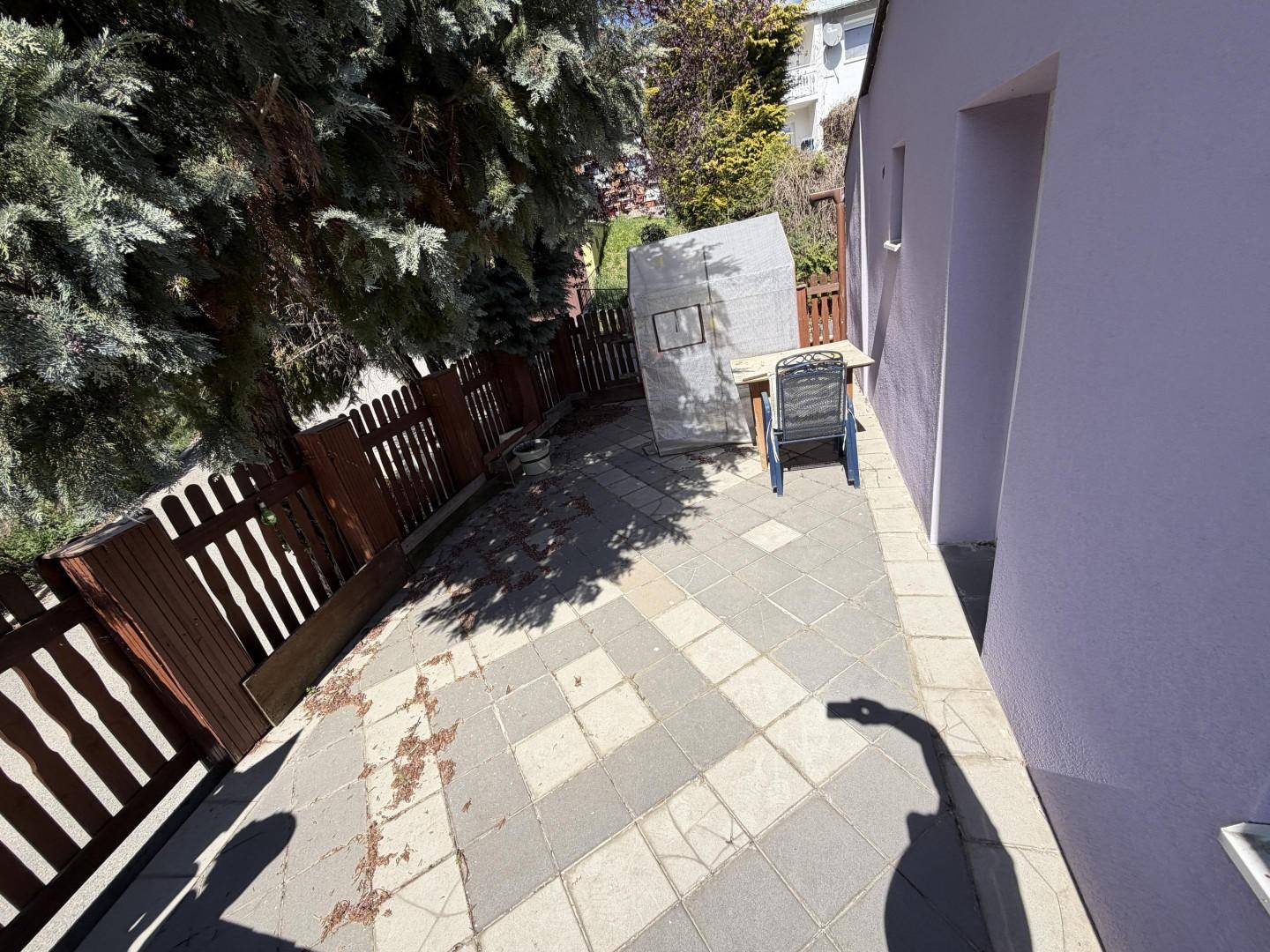 Terrasse mit Pflastersteinen, Holzzaun und viel Sonnenlicht.