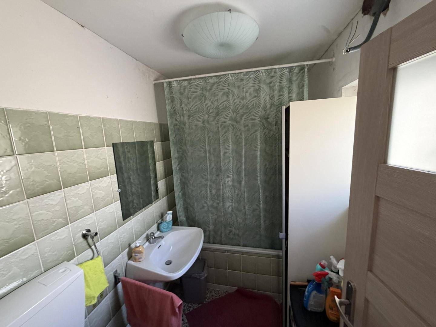 Badezimmer mit grünen und weißen Fliesen, Waschbecken und Duschvorhang.