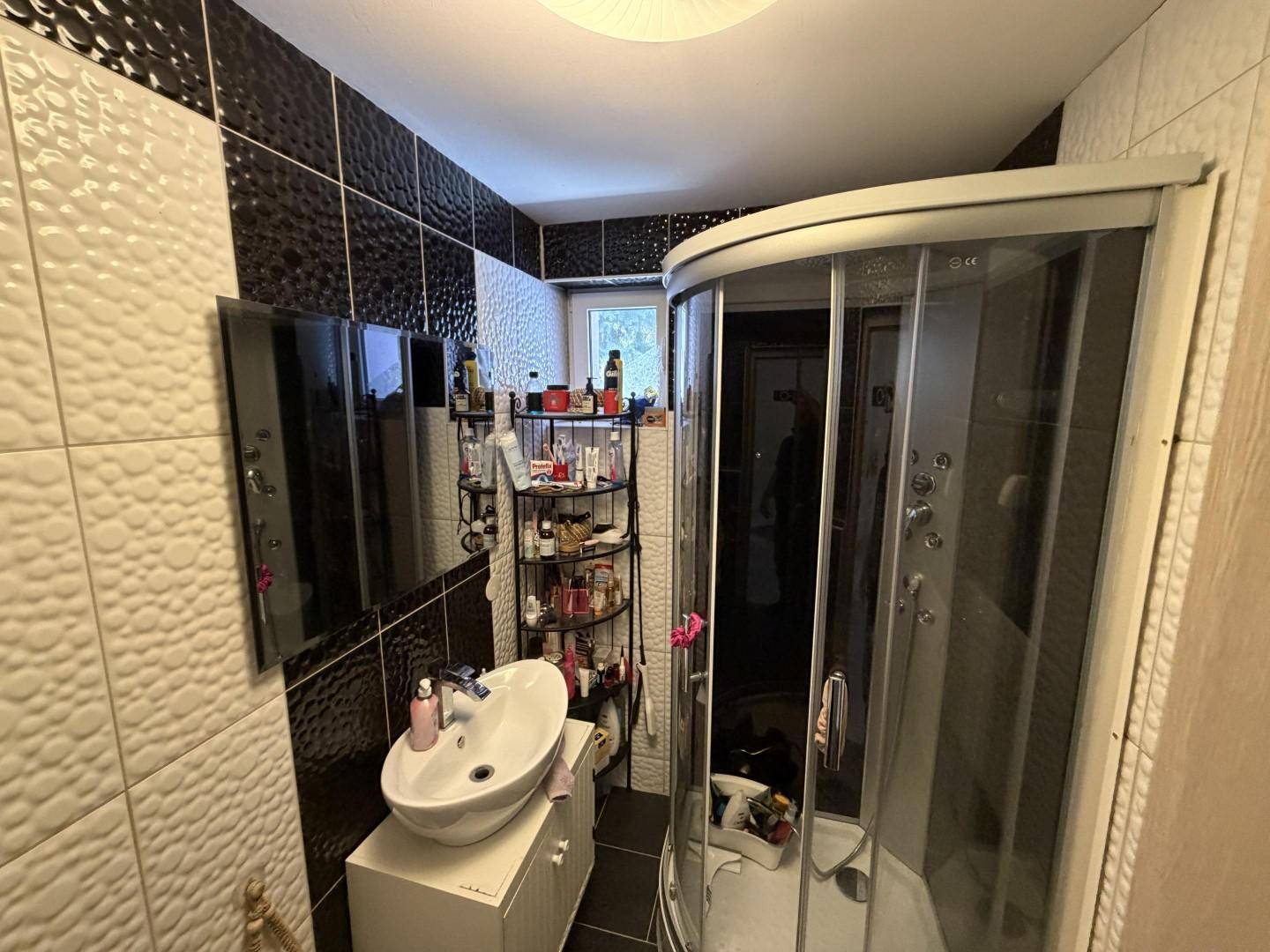 Badezimmer mit modernen schwarzen und weißen Fliesen, Duschkabine und Waschtisch.