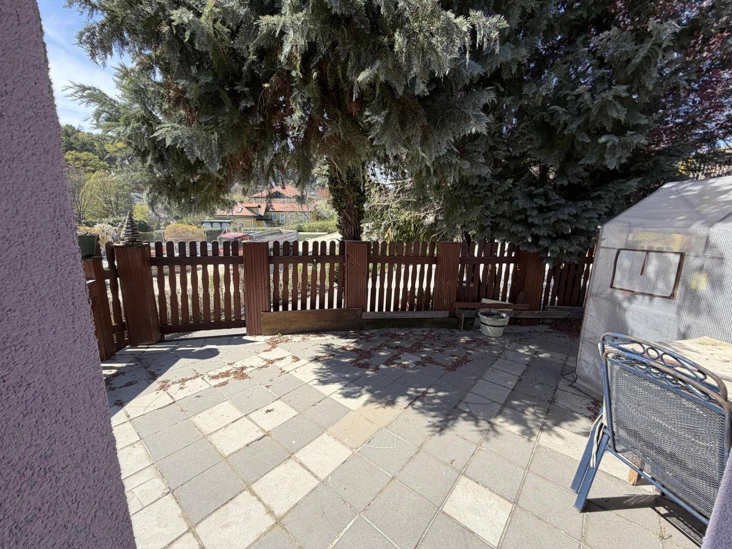 Gepflasterte Terrasse mit Holzzaun, Bäumen und Blick auf die Umgebung.