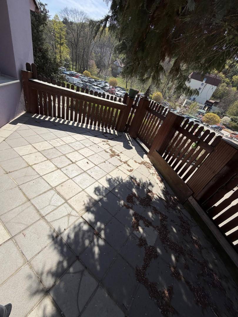 Gepflasterte Terrasse mit Holzzaun und Blick auf einen Parkplatz in der Ferne.