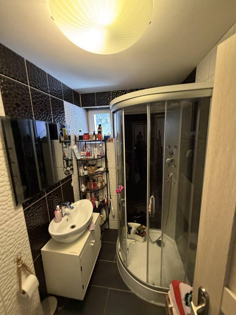 Modernes Badezimmer mit schwarzen und weißen Fliesen, Duschkabine und Waschbecken.