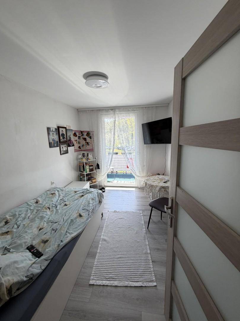Helles Schlafzimmer mit Einzelbett, Schreibtisch und Zugang zum Balkon.