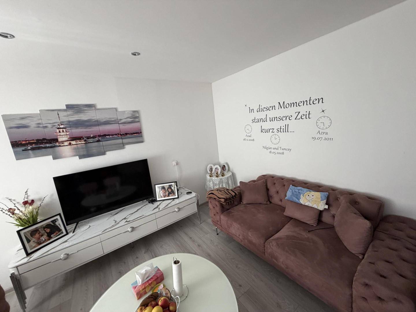 Gemütliches Wohnzimmer mit modernem Sofa, Fernseher und dekorativer Wandgestaltung.