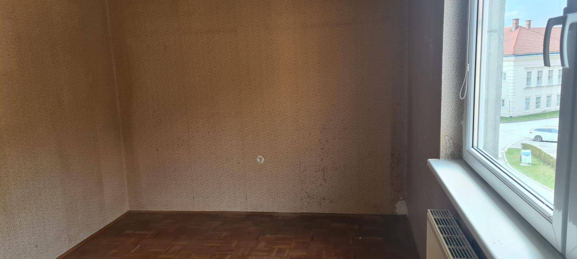 Leerer Raum mit Parkettboden, Fenster und Heizkörper, bereit zur Neugestaltung.