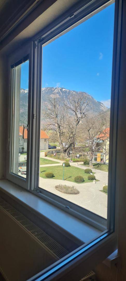 Fensterblick auf einen gepflegten Innenhof mit Bäumen und dahinterliegenden Bergen.