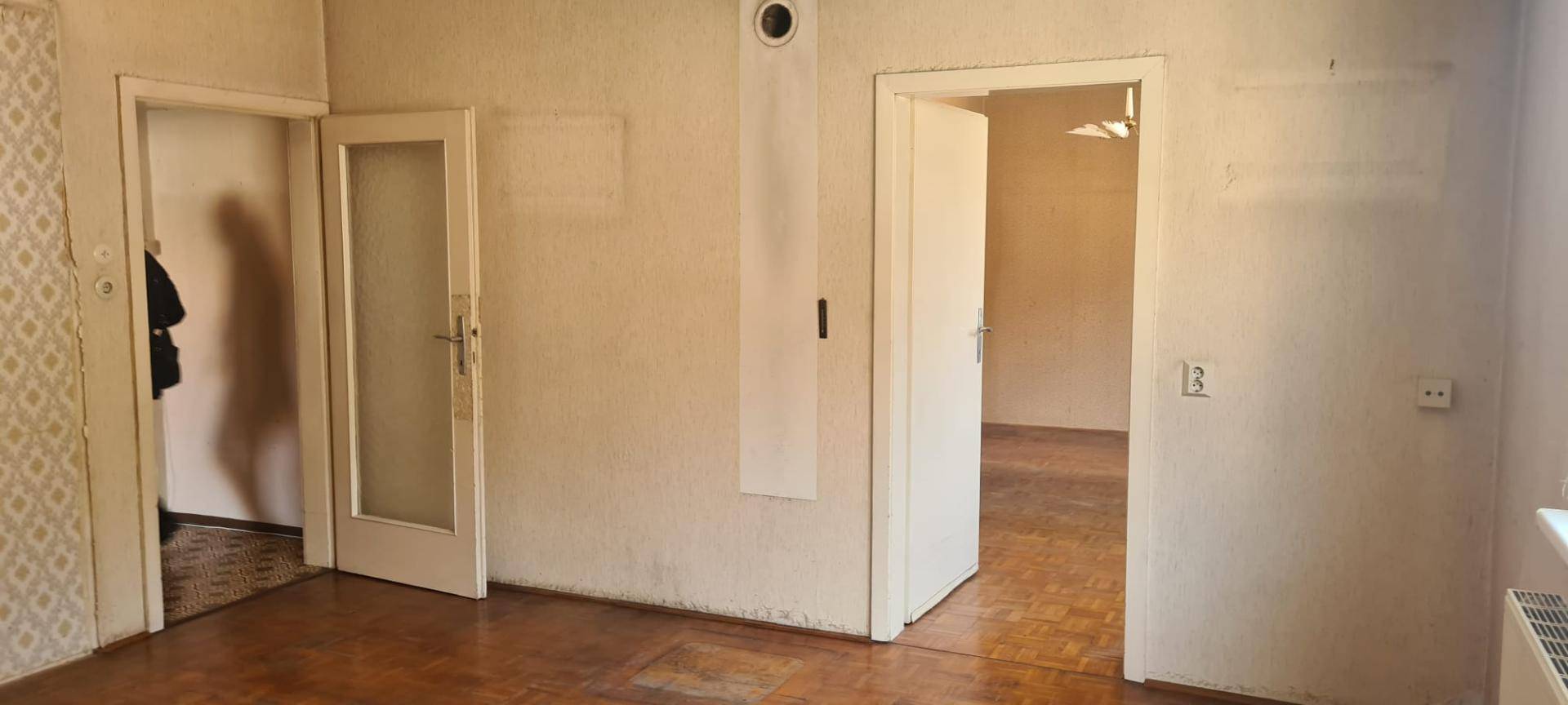 Leerer Raum mit Parkettboden und mehreren Türen, bereit für eine Renovierung.