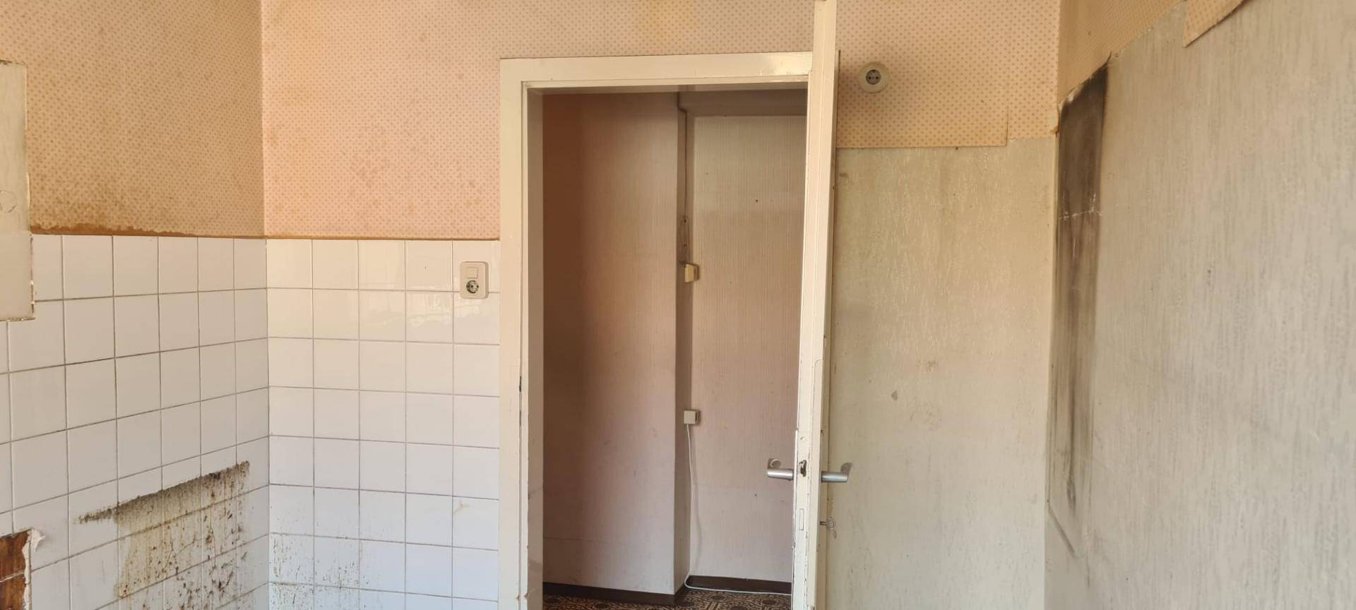 Renovierungsbedürftiger Raum mit alten Fliesen an den Wänden und abgenutzter Tapete.