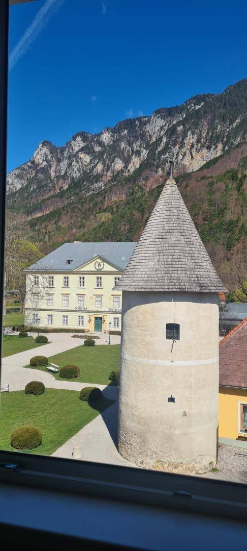 Fensterblick auf einen historischen Turm und ein großes Gebäude mit beeindruckender Bergkulisse.