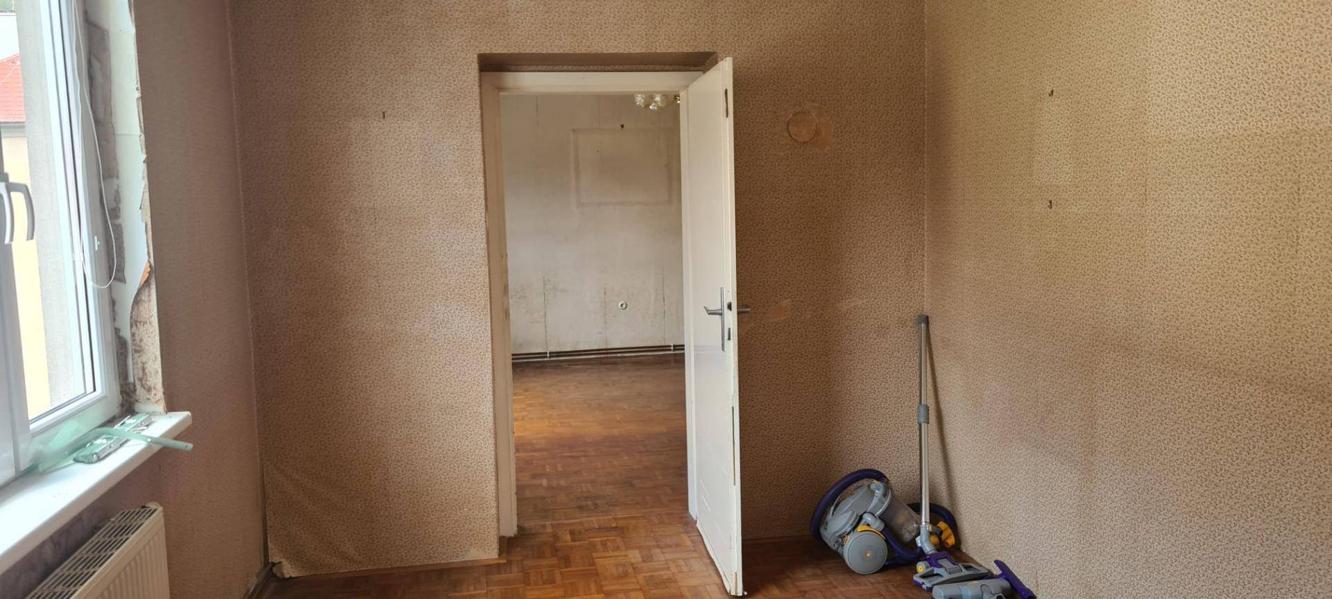 Leerer Raum mit Parkettboden und Fenster, der auf eine Renovierung wartet.