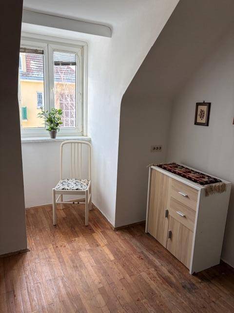 Heller Raum mit Fenster, Holzfußboden und einem kleinen Schrank.