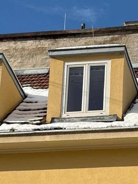Gelbe Fassade mit Gaubenfenster und schneebedecktem Dach an einem sonnigen Wintertag.