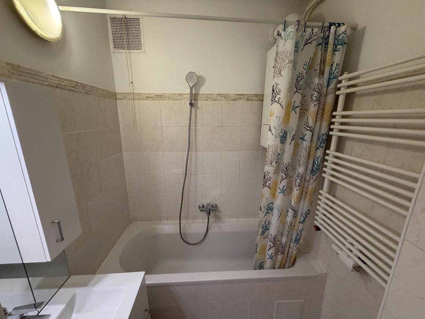 Funktionales Badezimmer mit Badewanne, Duschvorhang, Waschbecken und beheiztem Handtuchhalter.