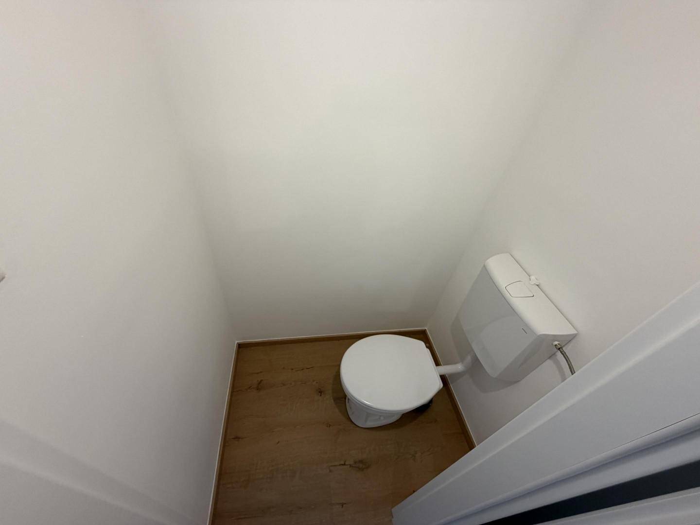 Kleines, funktionales WC mit einfacher Toilette und Holzboden.
