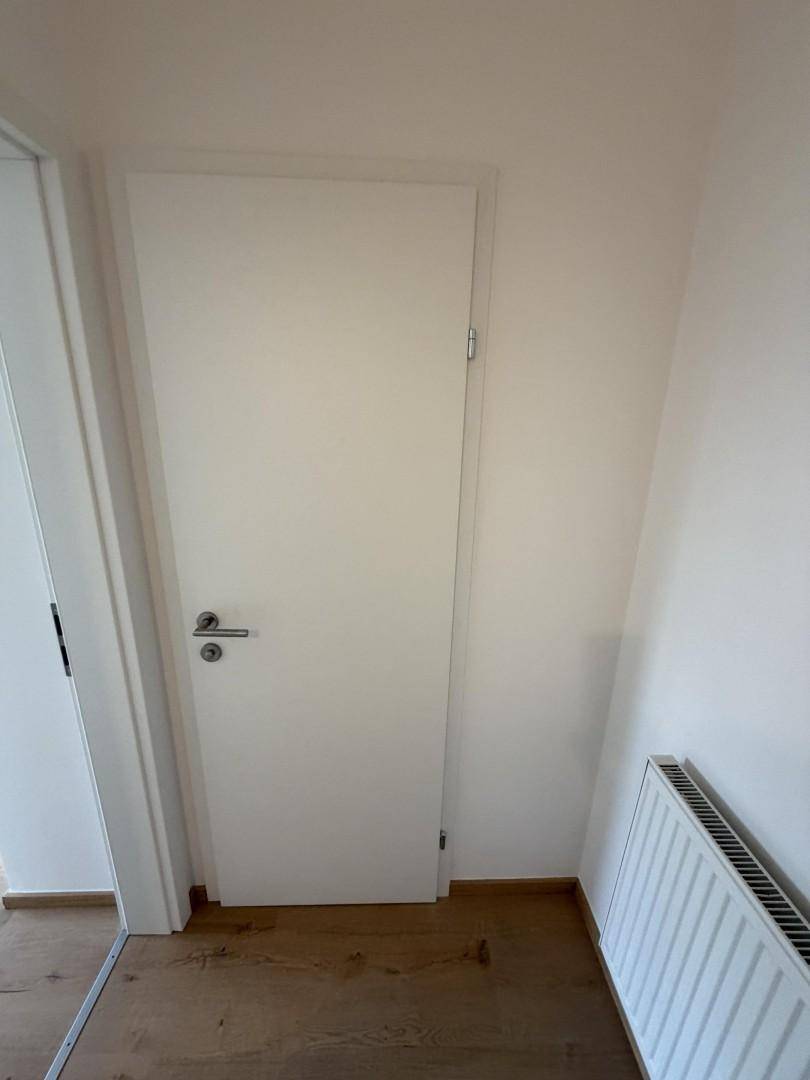 Weiße Tür in einem hellen Flur mit Holzboden und Heizkörper.