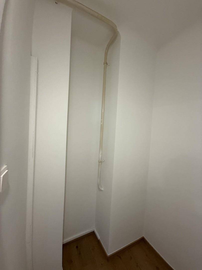 Kleiner Abstellraum mit sichtbaren Leitungen und Holzboden.