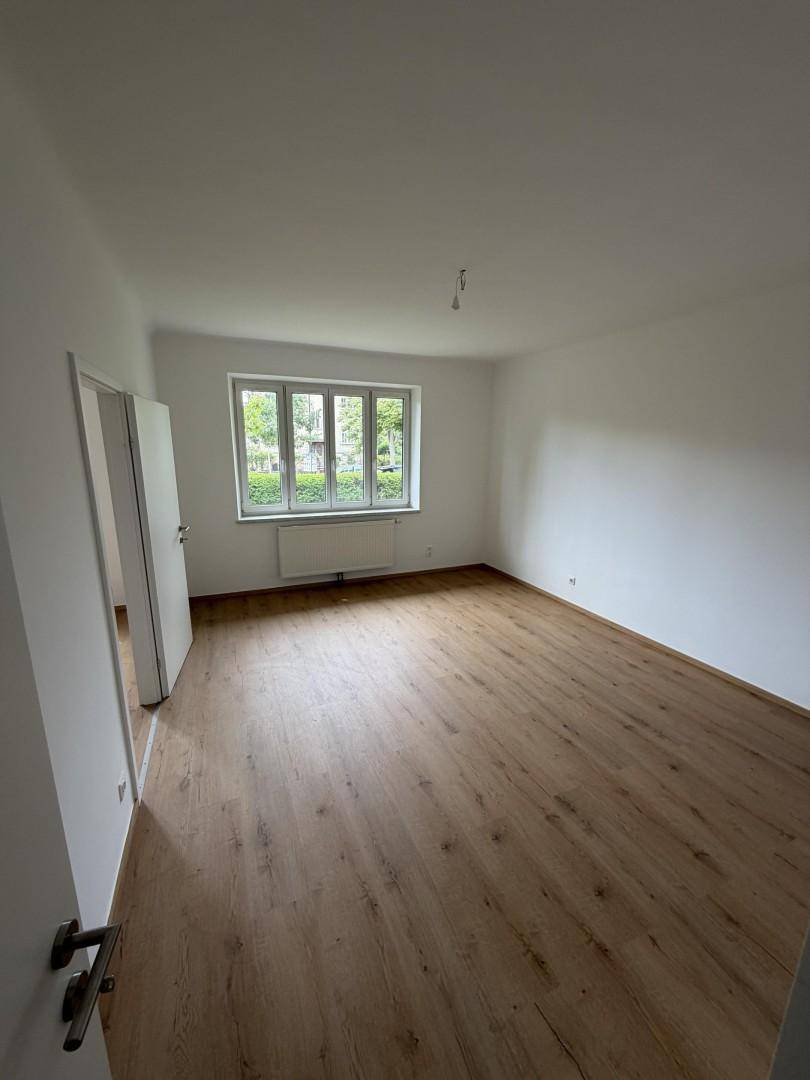 Geräumiges, helles Zimmer mit Holzboden und Fenster, das eine angenehme Wohnatmosphäre bietet.