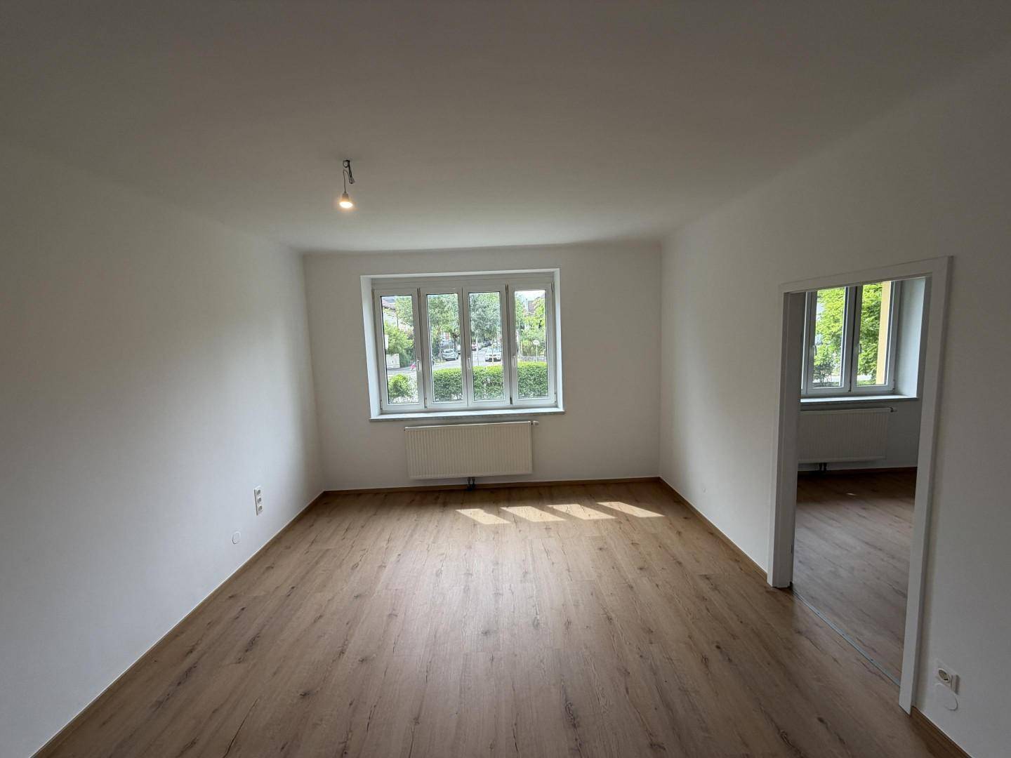 Geräumiges Wohnzimmer mit hellem Holzboden und Fensterfront zur Straße.