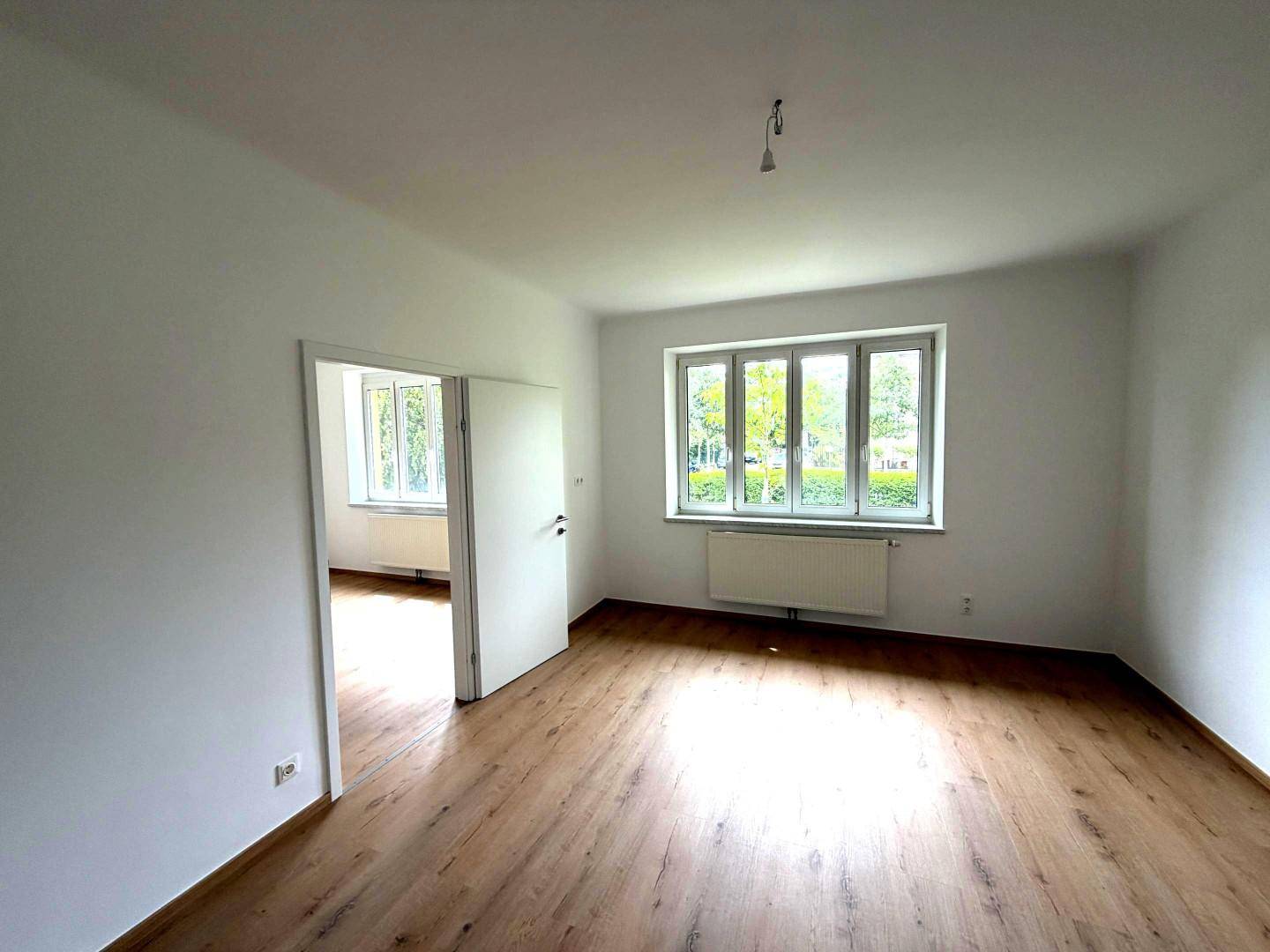 Helles Wohnzimmer mit Holzboden und Blick ins Grüne durch das Fenster.