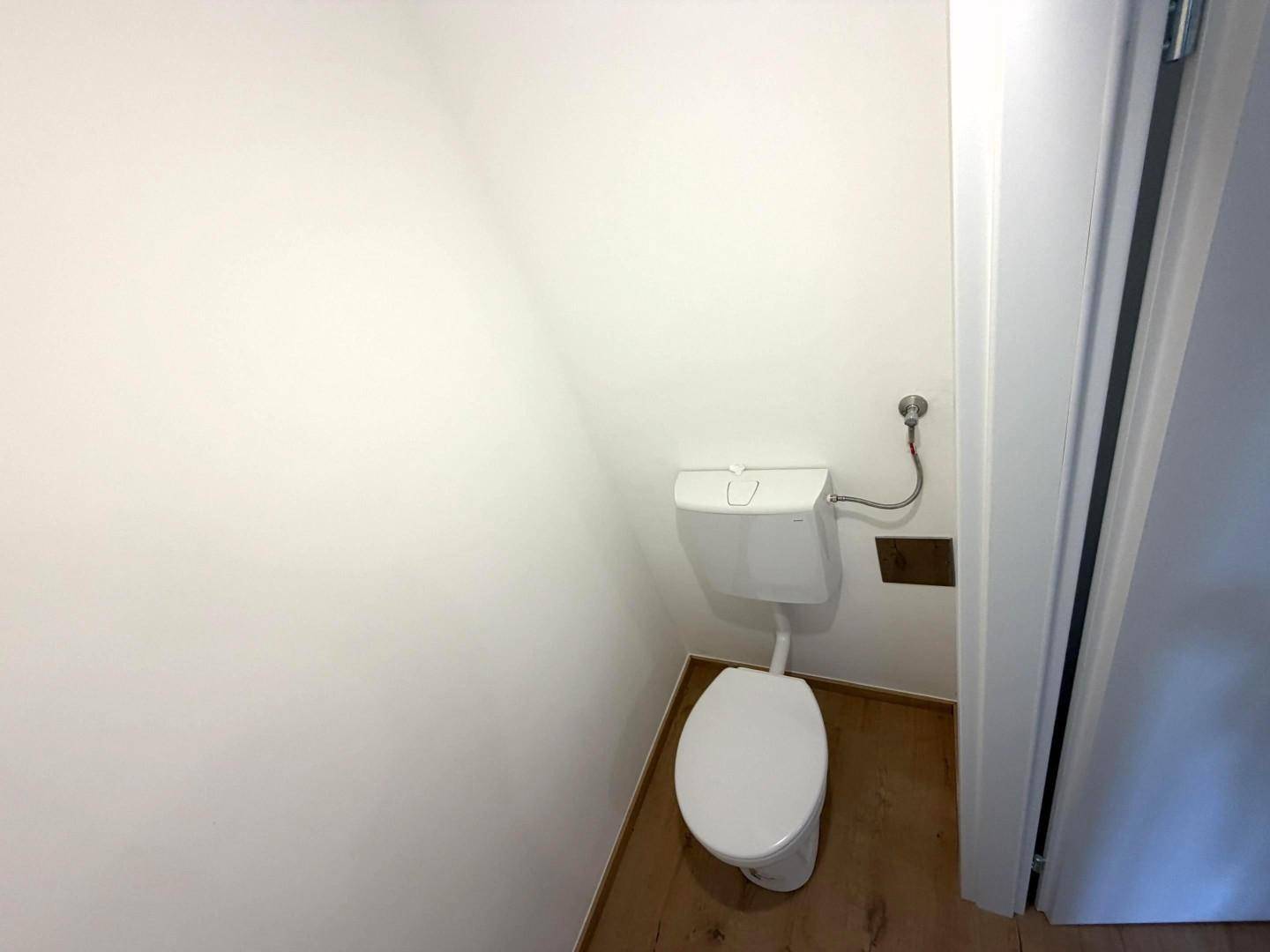 Schlichtes Gäste-WC mit Toilette und weiß gestrichenen Wänden.