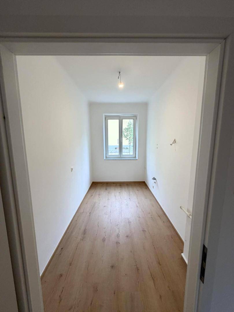 Schmaler, heller Raum mit Fenster und Holzboden, vielseitig nutzbar.