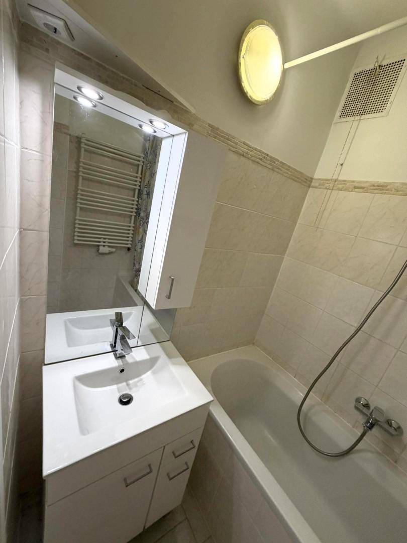 Badezimmer mit Badewanne, Waschbecken und Spiegelschrank, in beigen Fliesen gehalten.