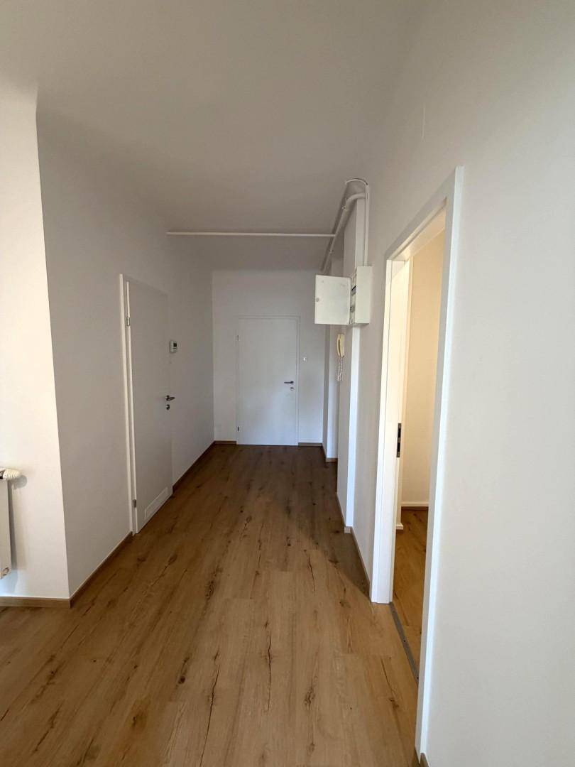 Langer Flur mit Holzboden, Elektrokasten und Zugang zu verschiedenen Räumen.