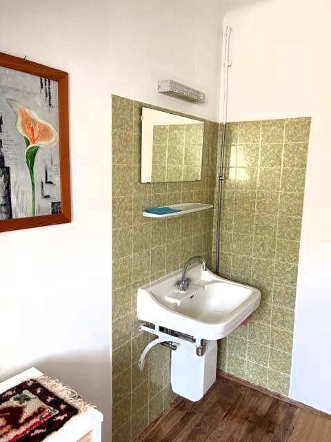 Kleines Badezimmer mit grün gefliesten Wänden, Waschbecken und Holzboden.
