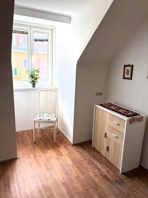 Heller Raum im Dachgeschoss mit schräger Decke, Fenster und Holzboden.