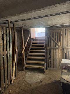 Kellerraum mit Holzverschlägen und einer Holztreppe, die nach oben führt.