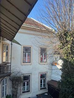 Ansicht eines älteren Gebäudes mit mehreren Fenstern und einem großen Baum im Vordergrund.