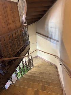Geschwungene Holztreppe mit schmiedeeisernem Geländer in einem historischen Gebäude.