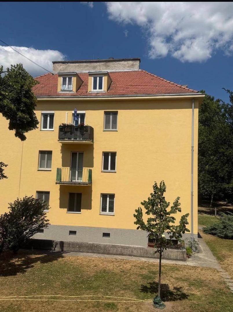 Ansicht eines gelben Wohngebäudes mit Balkonen und einem gepflegten Gartenbereich unter blauem Himmel.