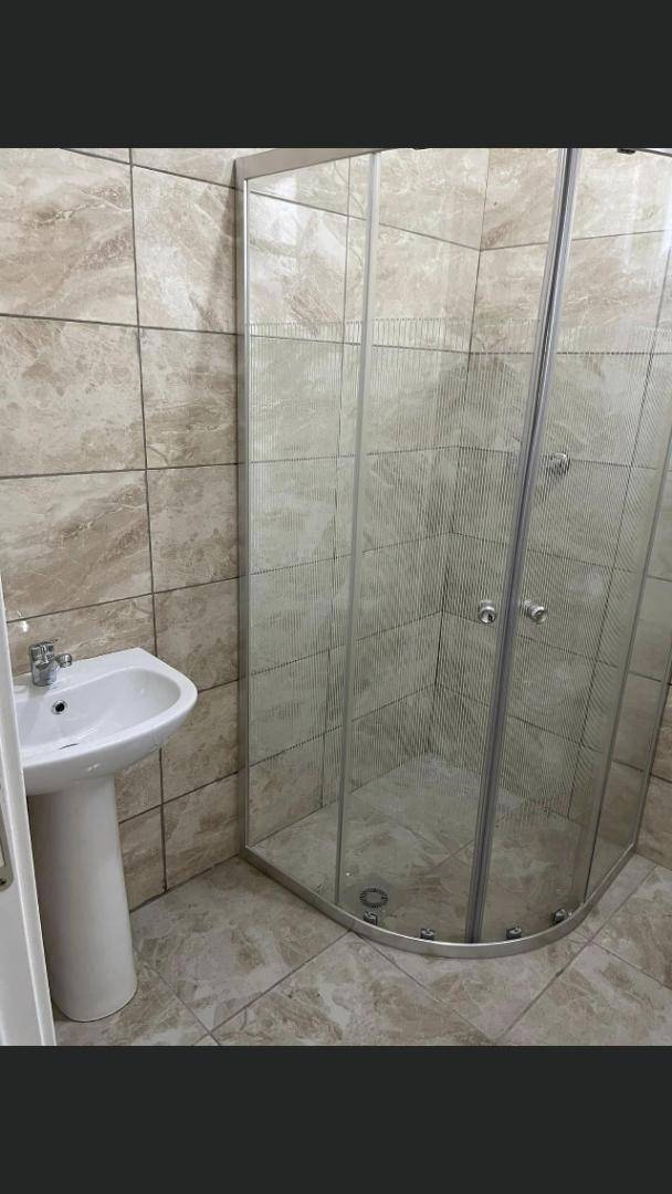 Badezimmer mit Duschkabine und einem einzelnen Waschbecken auf einem Standfuß.