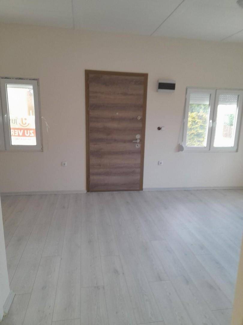 Leerer Raum mit Holztür, hellen Wänden und Laminatboden, bereit zum Einrichten.