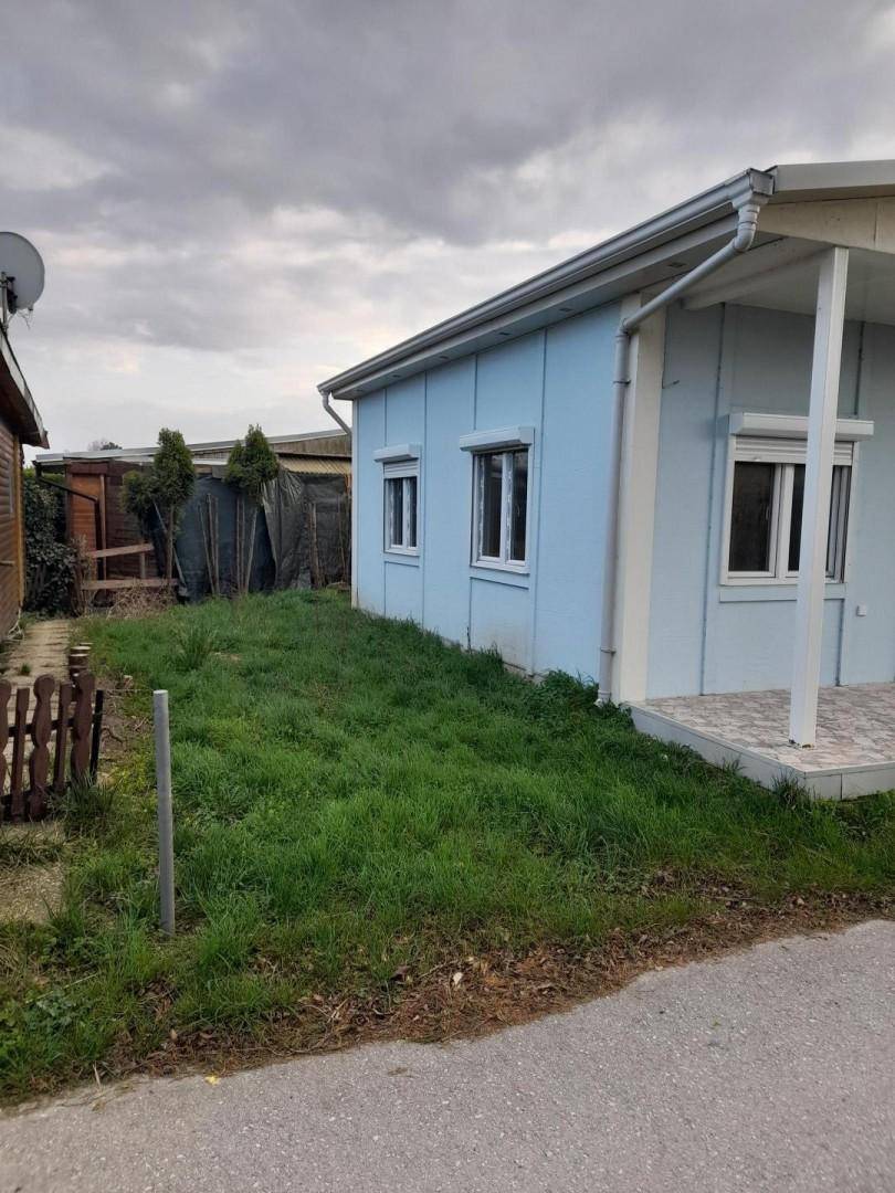 Blaues Haus mit kleinem Gartenbereich und einer gepflasterten Terrasse unter bewölktem Himmel.