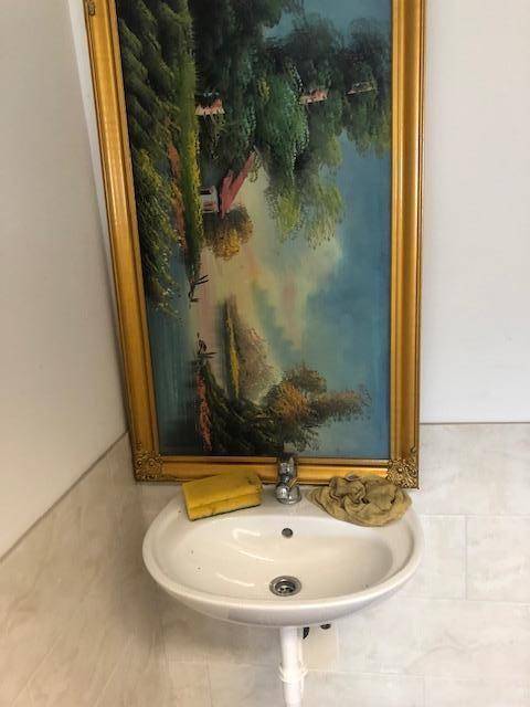 Kleines Waschbecken mit Wasserhahn unter einem großen, gerahmten Gemälde in einem gefliesten Raum.