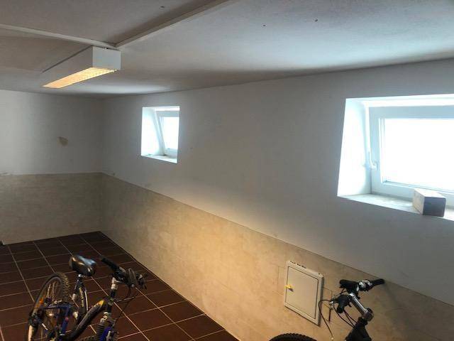Fahrradraum mit kleinen Fenstern, braunen Bodenfliesen und hellen Wandfliesen, beleuchtet von einer Deckenlampe.